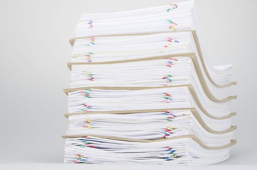 Overload of paperwork and brown envelope with colorful paperclip on white table.