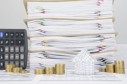 House and step pile of gold coins on finance account have calculator place vertical beside overload of paperwork and brown envelope with colorful paperclip as background.