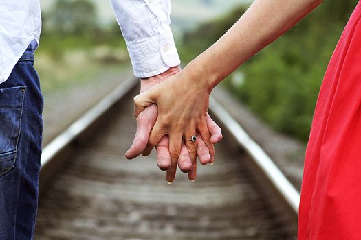 A couple walking hand in hand along a railroad track featuring an engagement ring.