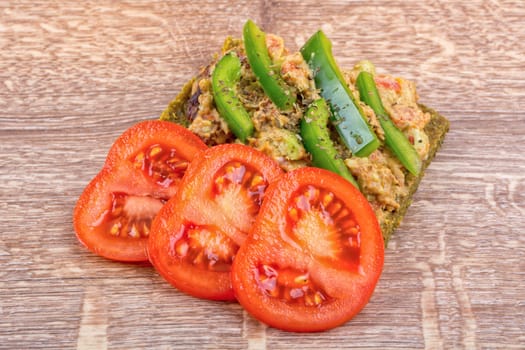 Raw bread with a spread decorated with green pepper and tomatoes