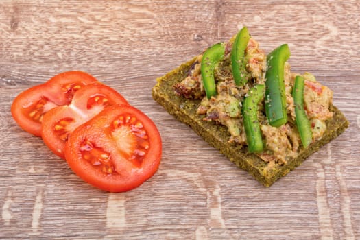 Raw bread with a spread decorated with green pepper and tomatoes