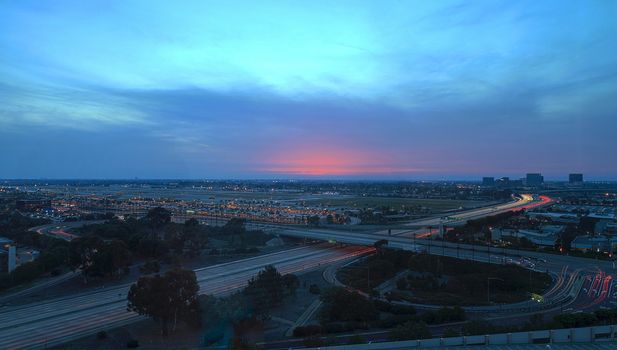 Aerial view of John Wayne Airport in Orange County, California, at sunset with rain in the air light trails across the 405 highway in front.