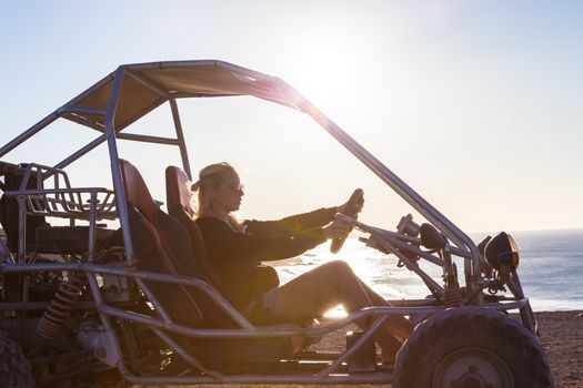 Active woman driving quadbike on dirt road by the sea in sunset.