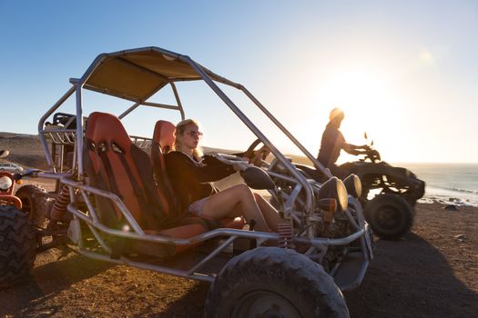 Active woman driving quadbike on dirt road by the sea in sunset.