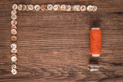 Sewing needle threaded with a orange thread ready for sewing. Buttons frame. Scene on a rustic wooden table. Top view with copy space.