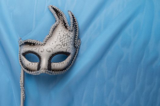 Colorful carnival mask on wavy blue satin fabric background.