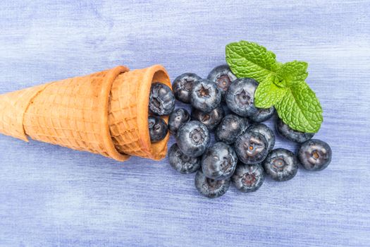 Waffle cones with blueberries and mint leaf on rustic textured background. Top view with copy space.