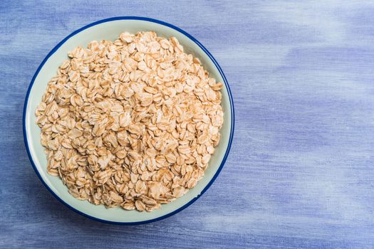 Oat flakes in a bowl on rustic textured background. Top view with copy space.