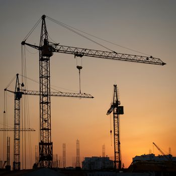 Industrial landscape with silhouettes of cranes on the sunset background