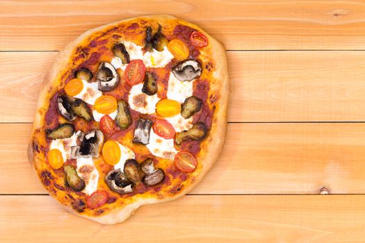 Top down view of freshly baked personal sized vegetarian pizza topped with mushrooms and yellow cherry tomatoes over wooden picnic table