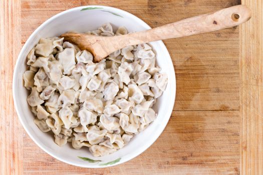 Top down perspective of wooden spoon in white pot full of delicious Turkish manti dumpling on table