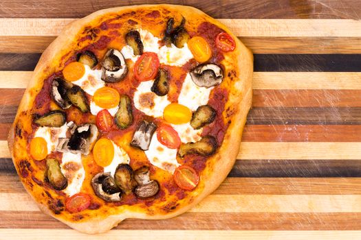 Single hand made cheese pizza with mushrooms and tomato slices over wooden striped cutting board