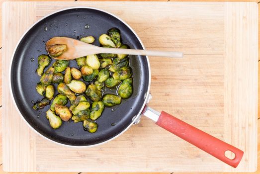 Top down first person view of delicious brussel sprouts cooked in non-stick pan with wooden spoon over cutting board