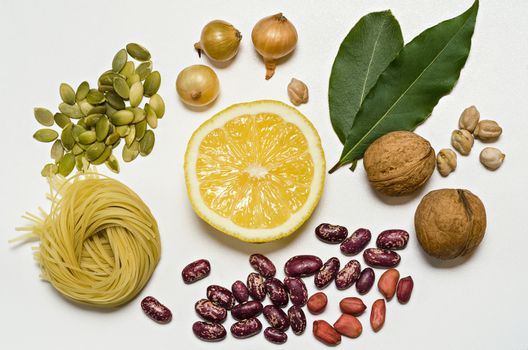 Pasta,half a lemon, beans, nuts and spices lie groups on a white background