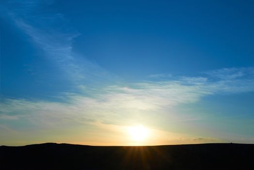 Mountains with colorful blue sky at sunset. Sun and clouds