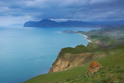 Sea harbor with blue water, green field and blue sky with clouds