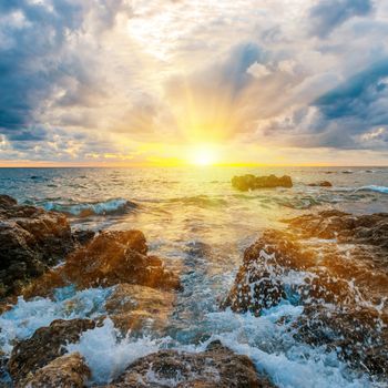 Sunset on the beach with waves, sea, rocks and dramatic sky