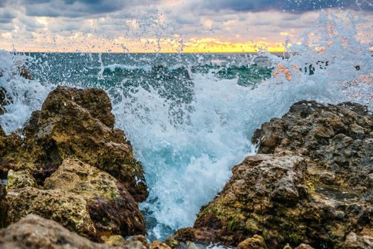 Sunset on the beach with waves, sea, rocks and dramatic sky