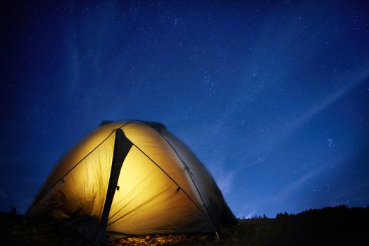 Illuminated yellow camping tent under stars at night