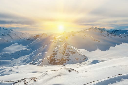 Sunset in snowy blue mountains with clouds. Winter ski resort