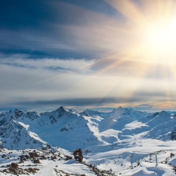 Sunset in snowy blue mountains with clouds. Winter ski resort