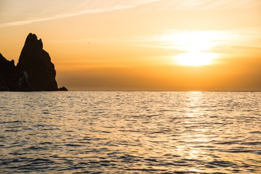 Sunset above the sea with rocks and orange sky