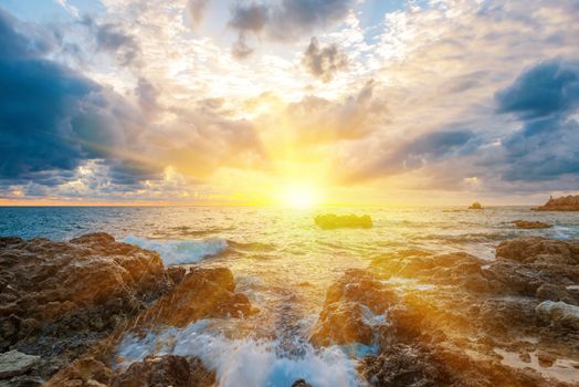 Sunset on the beach with waves, sea, rocks and dramatic sky. Landscape with sun in the centre