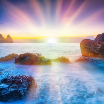 Sunset on the beach with sea, rocks and dramatic sky. Sunny landscape