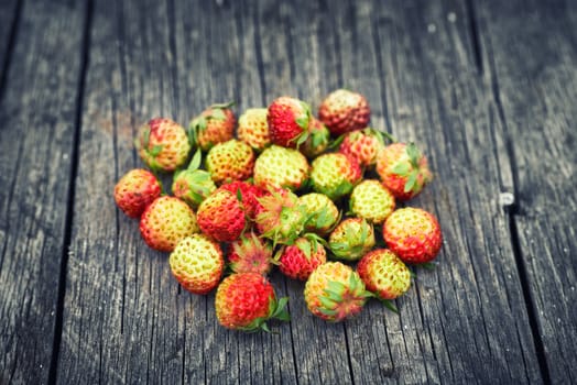 Bunch of red wild strawberry on the old wooden background