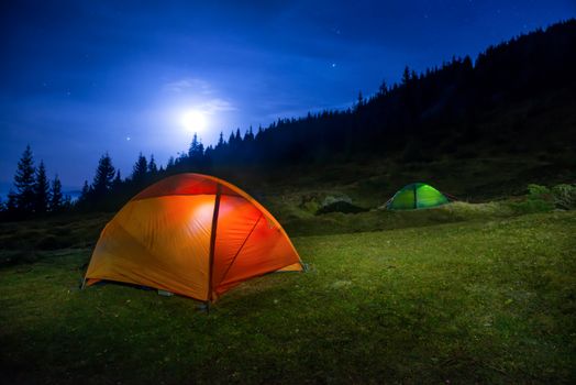 Two Illuminated orange and green camping tents under moon, stars at night