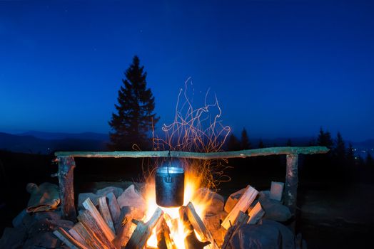 Cooking food in the pot on fire under blue night sky with many stars