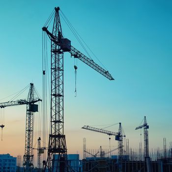 Industrial landscape with silhouettes of cranes on the sunset background