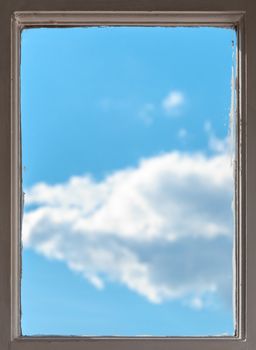 View of a clear sunny blue sky with fluffy white clouds through the wooden frame of an old window in a conceptual image