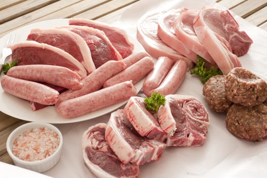 Raw pork and sausages with seasoning on white plates and wax paper ready for cooking outdoors