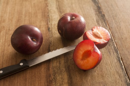 Three whole and cut raw plums with long knife knife on old brown wooden table table
