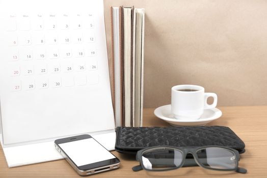 office desk : coffee with phone,stack of book,eyeglasses,wallet,calendar on wood background