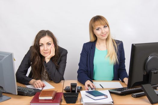 Two young beautiful girls colleagues sitting at the same desk in the office
