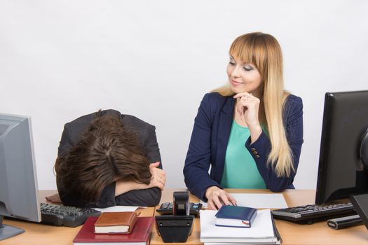 Two young beautiful girls colleagues sitting at the same desk in the office