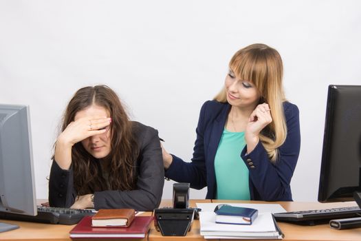 Two young beautiful girls colleagues sitting at the same desk in the office