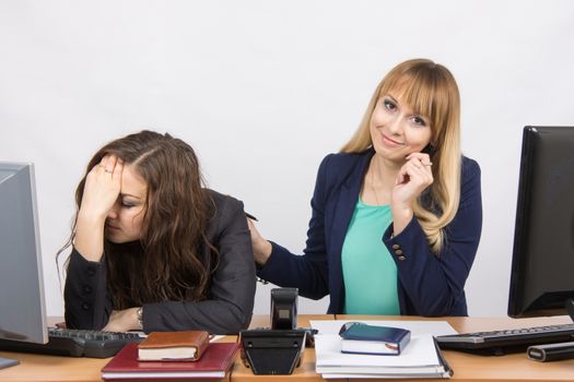 Two young beautiful girls colleagues sitting at the same desk in the office