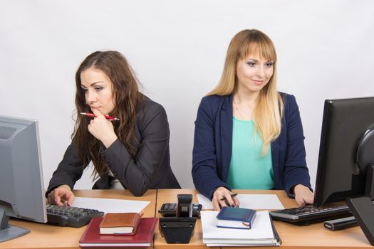 Two young beautiful girls colleagues sitting at the same desk in the office