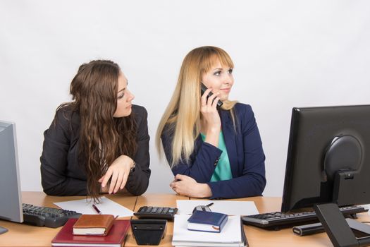Two young beautiful girls colleagues sitting at the same desk in the office