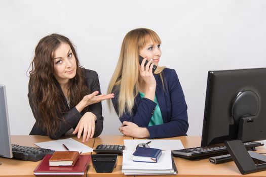 Two young beautiful girls colleagues sitting at the same desk in the office