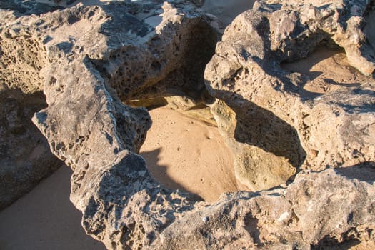 Rocks with sharp edges and holes on the beach of Atlantic Ocean in Morocco during the low tide. Enlightened hole with a soft sand in the bottom.