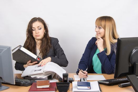 Two young beautiful girls colleagues sitting at the same desk in the office