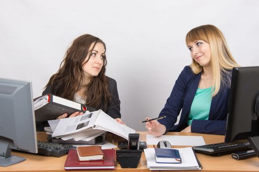 Two young beautiful girls colleagues sitting at the same desk in the office