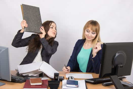 Two young beautiful girls colleagues sitting at the same desk in the office