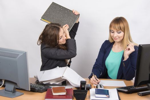 Two young beautiful girls colleagues sitting at the same desk in the office