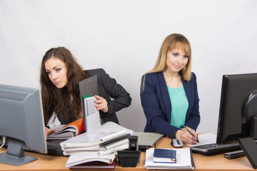 Two young beautiful girls colleagues sitting at the same desk in the office