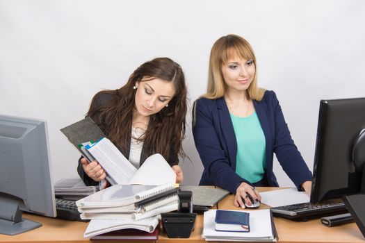 Two young beautiful girls colleagues sitting at the same desk in the office